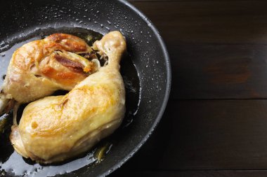 Koyu ahşap plakalar yakından görmek üzerinde siyah tavada iki kavrulmuş tavuk budu.