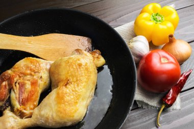 İki kızarmış tavuk budu siyah tavada sebze ve baharat üzerine koyu ahşap plakalar yakından görmek.