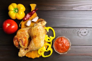 İki kızarmış tavuk ayak üzerinde kesme tahtası sebze ve baharatlar, koyu ahşap plakalar, üstten görünüm.