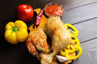 Sebze ve koyu ahşap plakalar, baharatlar ile kesme tahtası üzerinde iki kavrulmuş tavuk budu.