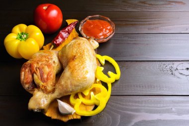 Sebze ve koyu ahşap plakalar, baharatlar ile kesme tahtası üzerinde iki kavrulmuş tavuk budu.