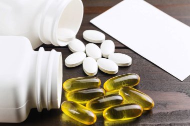 Sarı kapsüller omega 3, yağ asidi, balık yağı ve beyaz kalsiyum hapları, siyah tahta masa üzerinde beyaz kart, makro resim..