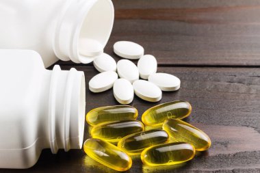 Sarı kapsüller omega 3, yağ asidi, balık yağı ve beyaz kalsiyum hapları, siyah ahşap masa üzerinde şişeler, makro resim.