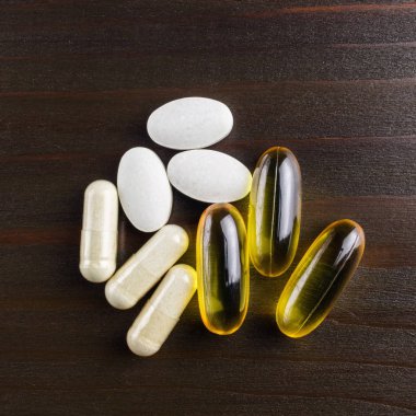 Vitamin ve beslenme takviyesi karışımı, sarı kapsüller omega 3, beyaz glukozamin, kalsiyum haplar ahşap masa, üst görüş..