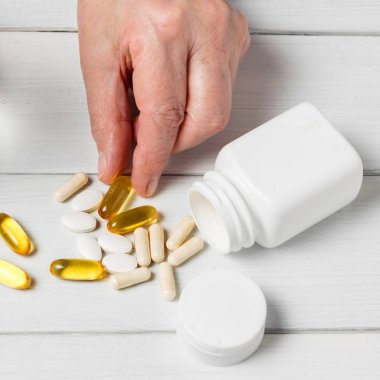 Kadın elleri sarı omega-3 kapsülleri, beyaz kalsiyum hapları, glukozamin takviyeleri ve tahta sehpalarda plastik şişe alır..