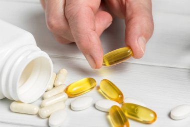 Kadın elleri sarı omega-3 kapsülleri, beyaz kalsiyum hapları, glukozamin takviyeleri ve tahta sehpalarda plastik şişe alır..