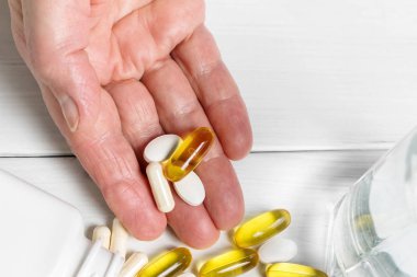 Kadın el bilgisayarı vitamin kompleksi ve beslenme takviyesi, sarı kapsüller omega 3, beyaz kalsiyum ve glukozamin hapları, bir bardak su ahşap masa..