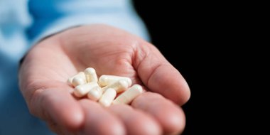 Beyaz ilaç kapsülleri glukozamin, kadın avuç içinde sağlıklı destek hapları, siyah arka planda..