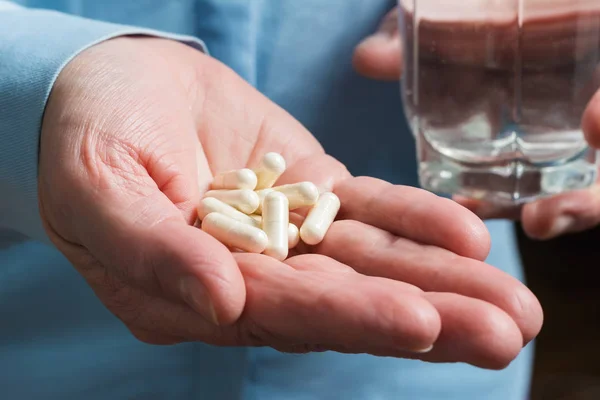 Beyaz ilaç kapsülleri glukozamin, kadın avucunda sağlıklı takviye hapları ve diğer elinde su olan bardak..