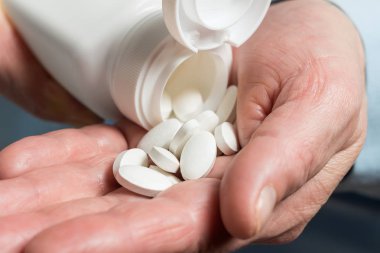 Kadın elinde beyaz ilaç hapları, beyaz bir şişeden kalsiyum tabletlerinin diyet takviyesine dökülüyor..