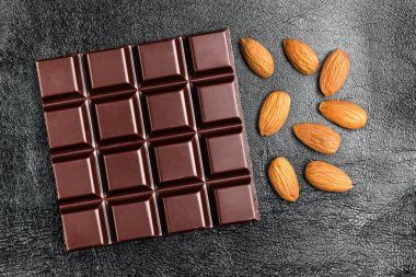 Karanlık, acı çikolata bar ve badem fındık siyah deri arka plan, üstten görünüm doku.