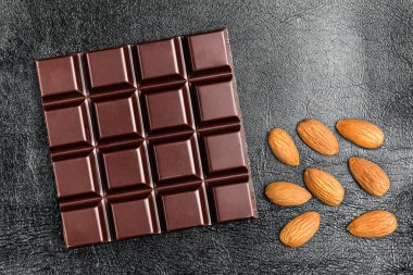 Karanlık, acı çikolata bar ve badem fındık siyah deri arka plan, üstten görünüm doku.