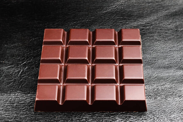 Dark, bitter chocolate bar on black leather texture background.