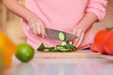 Kadın elleri bıçakla salatalık kesiyor.