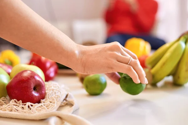 Mulher mãos segurando limão verde com outras frutas no fundo — Fotografia de Stock