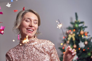 Arka planda Noel ağacı olan bir kadın kameraya gülümsüyor.