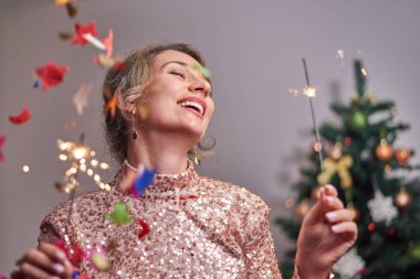 Arka planda Noel ağacı olan bir kadın kameraya gülümsüyor.