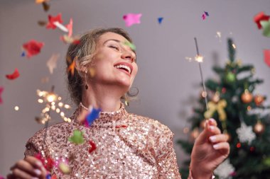 Arka planda Noel ağacı olan bir kadın kameraya gülümsüyor.