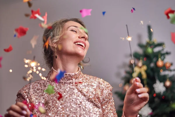 Arka planda Noel ağacı olan bir kadın kameraya gülümsüyor.