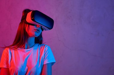 Beyaz tişört giyerken elinde sanal gerçeklik kaskı tutan genç bir kız.