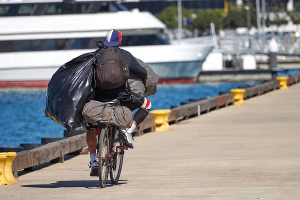 Homem sem-teto andando de bicicleta enquanto carrega sacos e mochilas — Fotografia de Stock