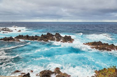 Portekiz 'in Madeira adasının kayalık Atlantik kıyısında huzursuz, berrak, mavi suyu ve kayalıkların dibinde bir sürü köpükle çekilmiş.