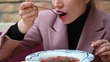 Woman in pink suite eating red vegetable soup at business lunch