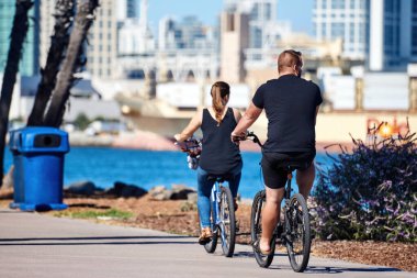 SAN DIEGO, CALIFORNIA - SEPTEMBER 30, 2019: Mature couple riding bike in the park. Cargo port on background