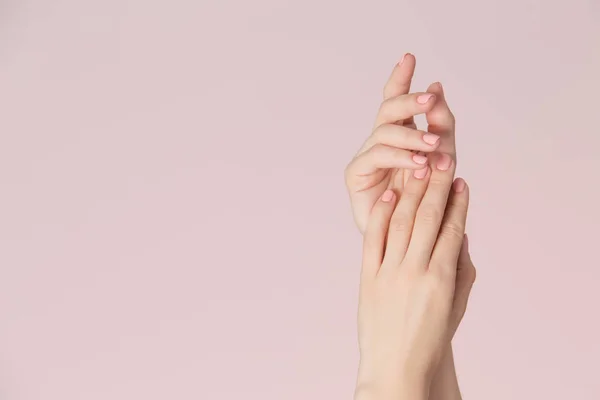 Kadın temiz cilt ile elleri ve pembe Lehçe manikür üzerinde pembe bir arka plan ile çivi. Tırnak bakımı ve güzellik Tema. Güzellik arka plan kopya alanı ile.