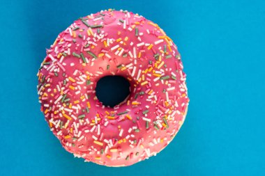 Mavi arka planda izole edilmiş, üzerinde renkli süslemeler olan pembe şekerli donut.