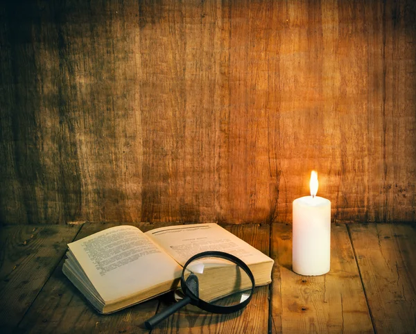 Nyitott könyv, és egy fehér gyertya egy fából készült asztal. Olvasása a gyertyafénynél. Vintage összetétele. Szabad hely, a szöveg. Ókori könyvtár. Antik irodalom. — Stock Fotó