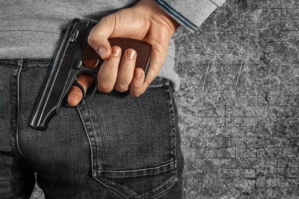 Ein Mann mit einer Waffe in der Hand hinter seinem Rücken, Nahaufnahme. Begriffe: Verbrechen, versuchter Mord, eine Schusswunde, der Mörder, Raub. — Stockfoto