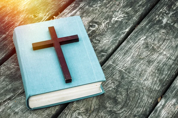 Closeup of wooden Christian cross on bible, burning candle and prayer beads on the old table. Church utensils. — Stockfoto