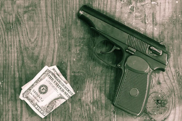 The gun and money on wooden table. Concepts: crime, contract killing, killer, robbery, extortion, money laundering.