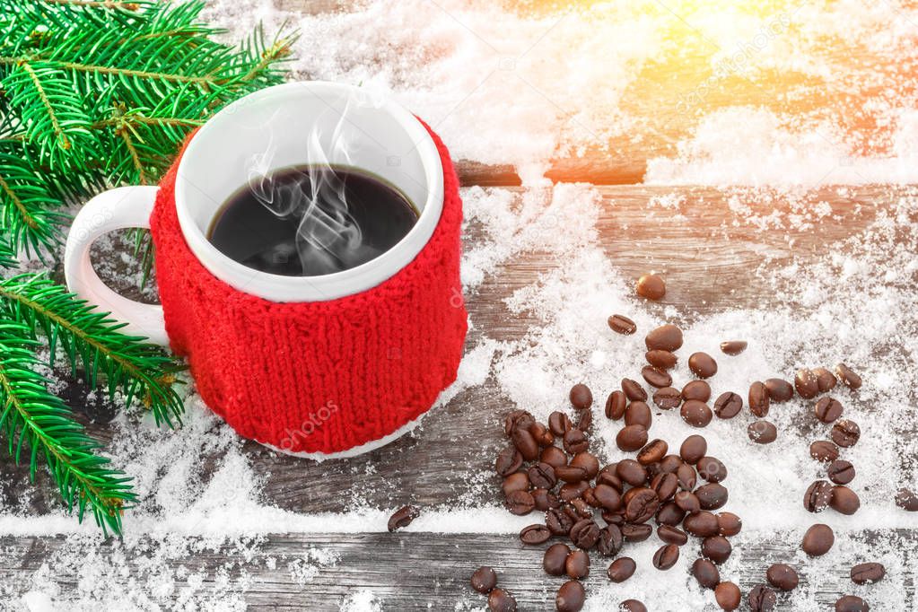 Cup of hot coffee on the old snowy table and christmas tree branch in sunshine, coffee beans. Feeling of comfort and holiday mood. Xmas and New Year fairy tale background. Beautiful greeting card.