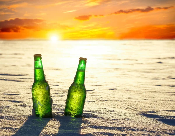 Deux bouteilles de bière fraîche sur la neige au coucher du soleil. Vue rapprochée . — Photo