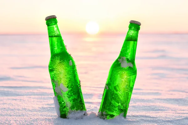 Deux bouteilles de bière fraîche sur la neige au coucher du soleil . — Photo