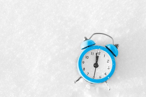 Vintage alarm clock on the snow at sunset. The concept of Christmas and New Year. Magic composition. Switched to winter time. Good morning. Waiting of holiday.