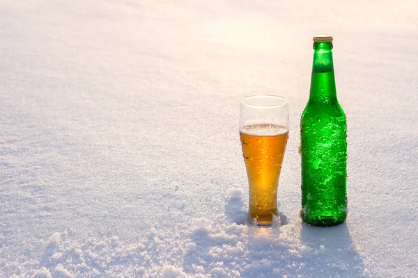 Bögre és üveg hideg sört a hóban, a naplemente. Gyönyörű téli háttér. Szabadtéri kikapcsolódást. Alkoholtartalmú italok reklámozására. — Stock Fotó