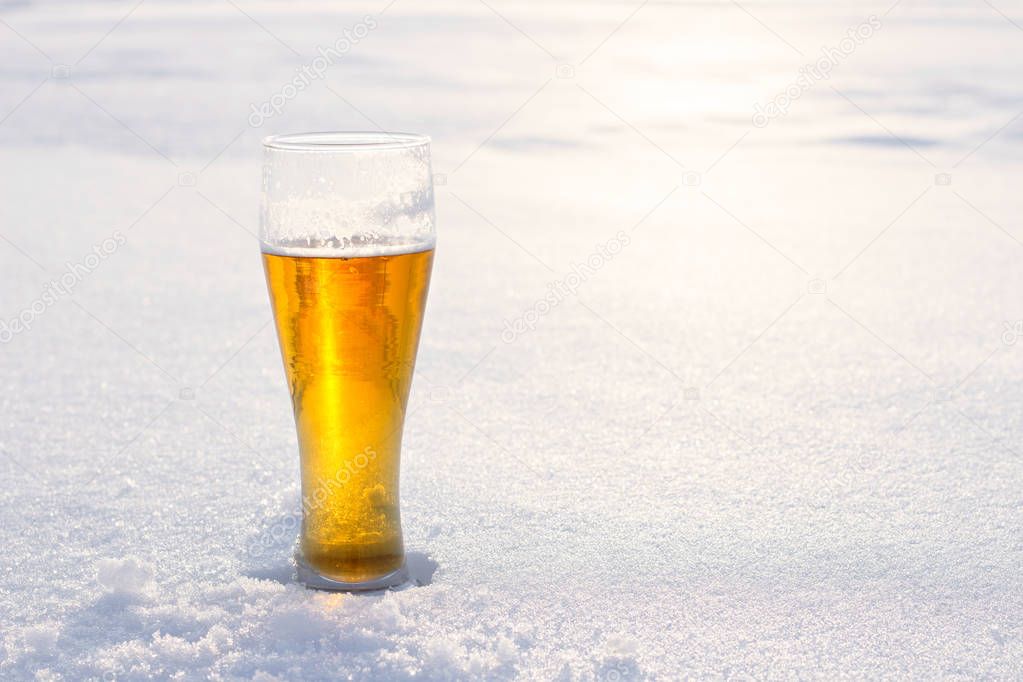 Mug of cold beer in the snow at sunset. Beautiful winter background. Outdoor recreation. Advertising of alcoholic beverage.