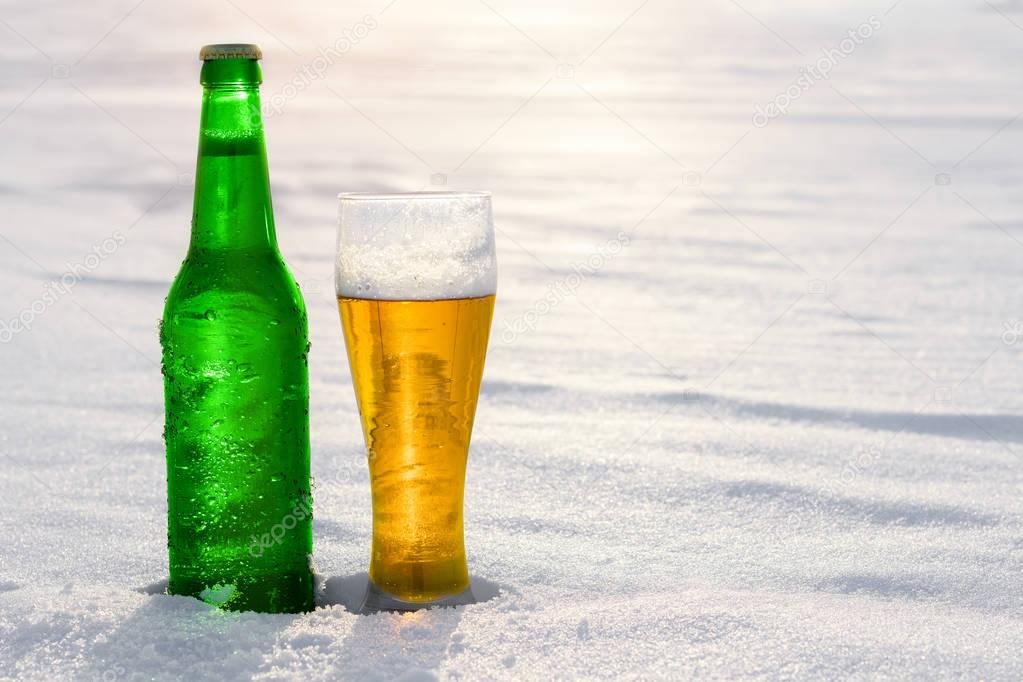 Mug and bottle of cold beer in the snow at sunset. Beautiful winter background. Outdoor recreation. Advertising of alcoholic beverage.