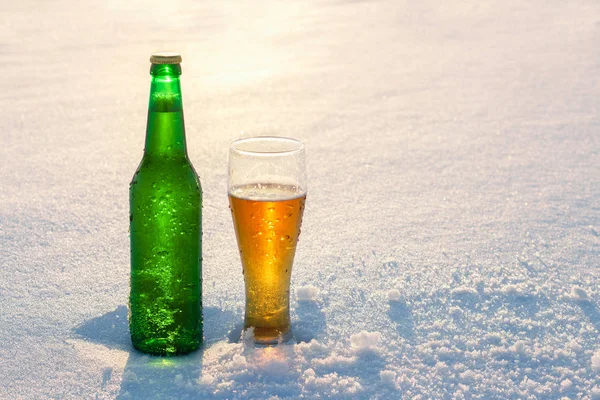 Taza y botella de cerveza fría en la nieve al atardecer. Hermoso fondo de invierno. Recreo al aire libre. Publicidad de bebidas alcohólicas. Bebida y vacaciones . —  Fotos de Stock