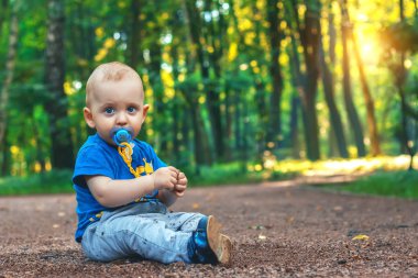Küçük şirin Bebek meme başı ile patika rüya gibi ormanda tek başına oturur. Yerde oturan ve parkta oynarken küçük çocuk. Güzel doğa günbatımı vasıl geçmiş. Yaz ruh hali.