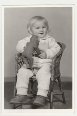 Vintage Fotoğraf küçük bir girk hasır koltuğa oturur ve peluş oyuncak (oyuncak) tutar gösterilir. Retro siyah ve beyaz fotoğraf.