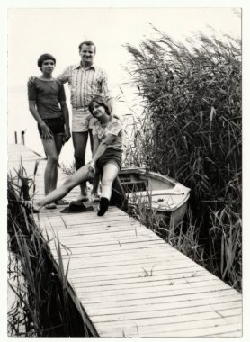 Vintage photo shows father and adolescent (teenager) children pose on the pier. The pier and boat - summer holidays (vacation) theme.  clipart