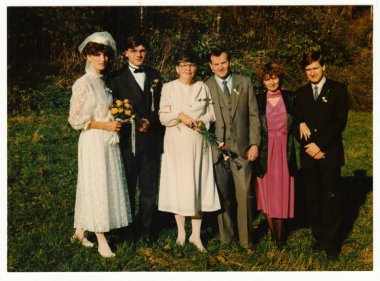 Retro fotoğraf yeni evliler ve düğün Konuklar açık havada poz gösterir. Gelin beyaz narin gelinlik giyer. O küçük bir altın gül buketi sahiptir. Vintage renkli fotoğraf.