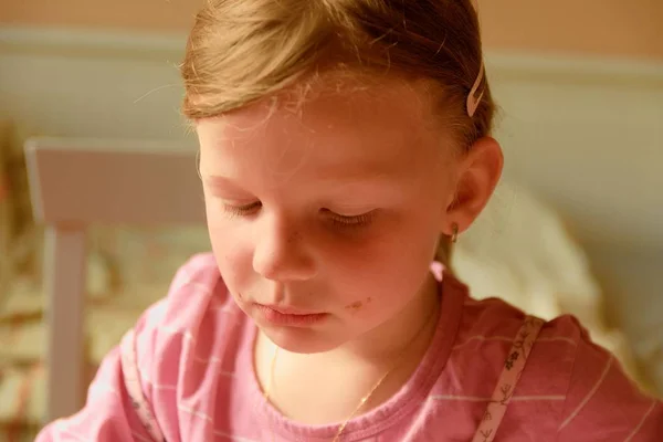 Uma menina pequena bonito triste. Uma menina pequena olha tristemente para baixo. Uma menina pequena senta-se na cozinha . — Fotografia de Stock