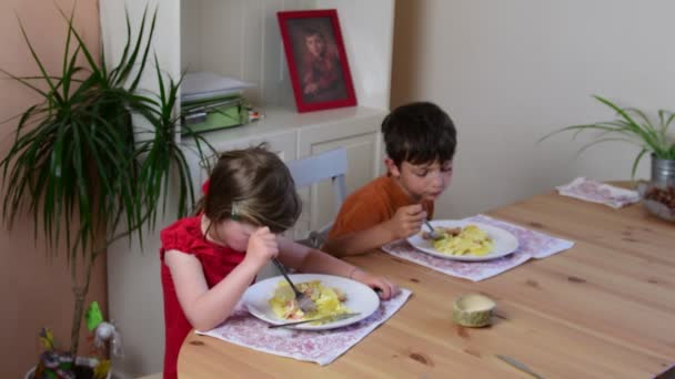 Linda niña y su hermano se comen la cena. Los niños comen en la cocina. Niña y niño en la cocina. Chica se niega a su cena . — Vídeos de Stock