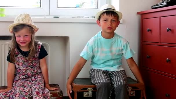 Söt liten flicka och en pojke sitta på vintage resväskor och vänta på Start holiday. Small tjej bär blommiga klänning. Reser koncept — Stockvideo