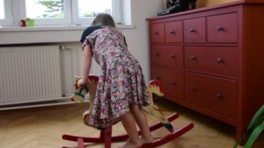 Sevimli küçük kız üzerinde sallanan at sallanır. Smalll kız çiçekli elbise giyer. Çocukluk kavramı